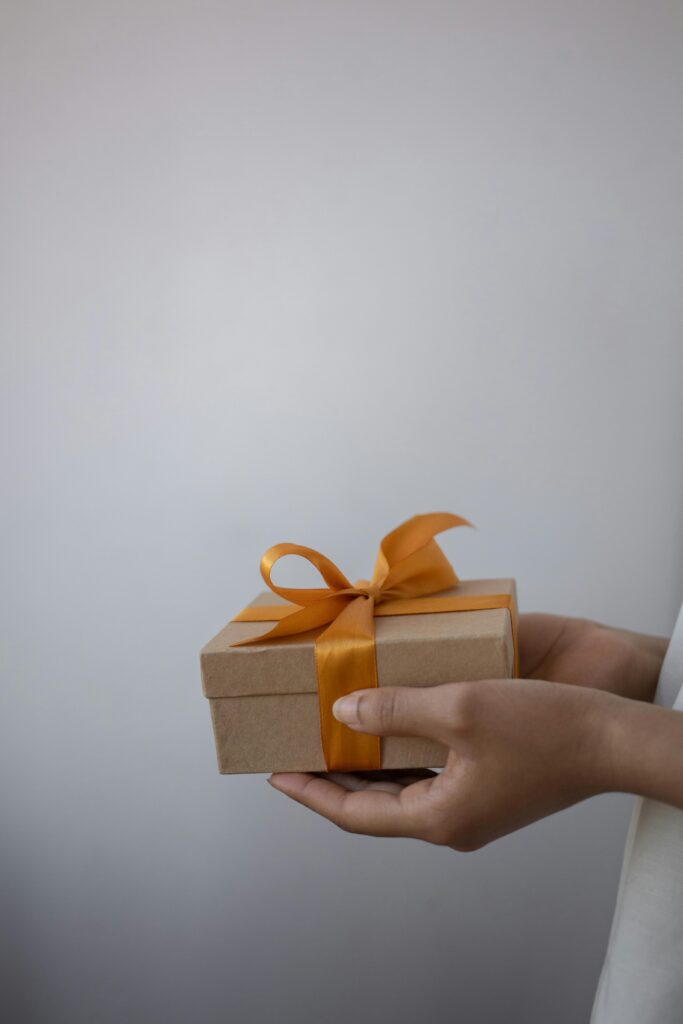 A close-up of hands holding a gift box decorated with an orange ribbon bow.